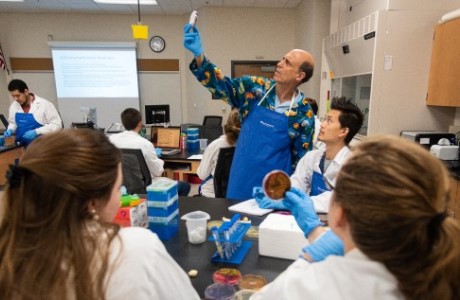 Professor in a classroom holding up sample while a student looks on