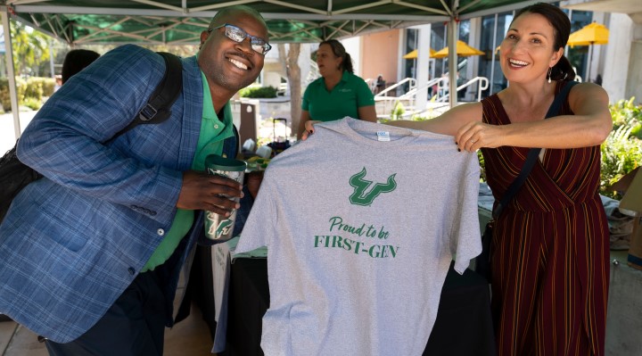 A smiling man and woman who is holding up a USF First Gen t-shirt.