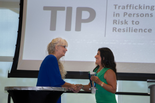 Two women shaking hands in front of projector that reads "TIP"