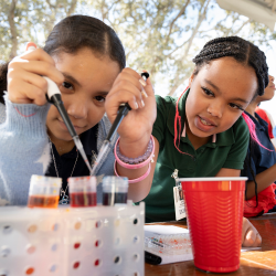 Two children working on a science experiment involving beakers and droppers