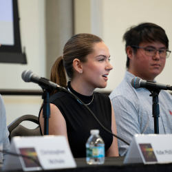 Two students speaking on a panel in front of microphones