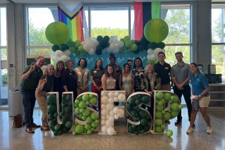 People posing in front of a USF sign filled with green and white balloons