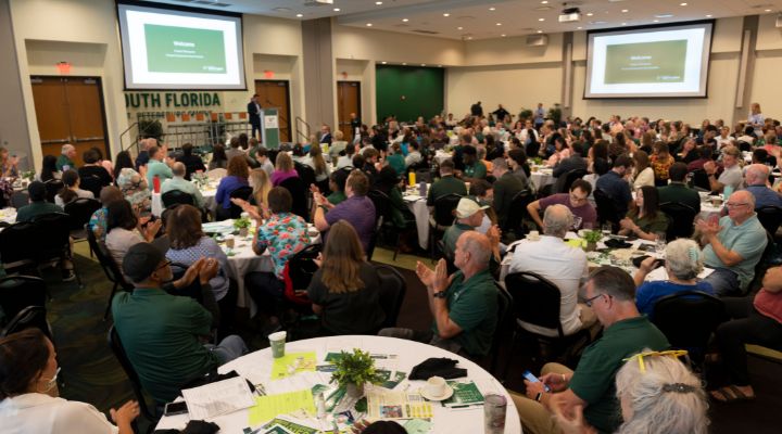 Large group of people in ballroom for event with tables and speaker