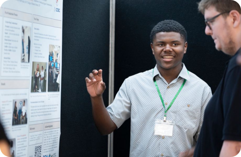 A student standing in front of an academic poster explaining the board.