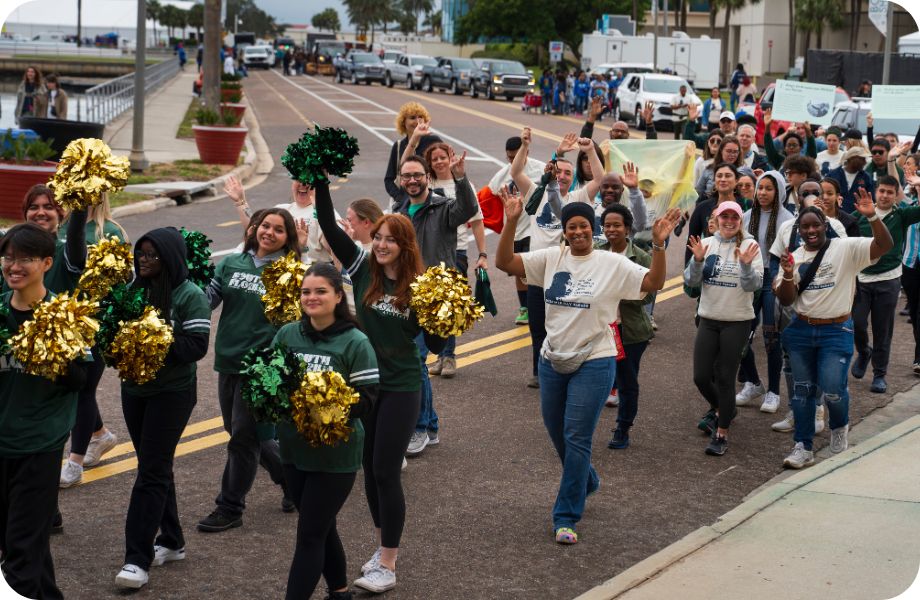 Group of people, including USF cheerleaders with pom-poms, walkning in a parade