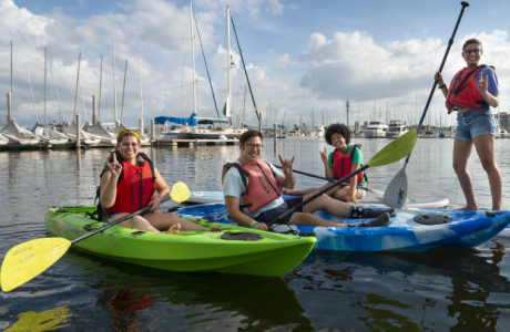 Students on kayaks and paddle boards making a Go Bulls hand sign.