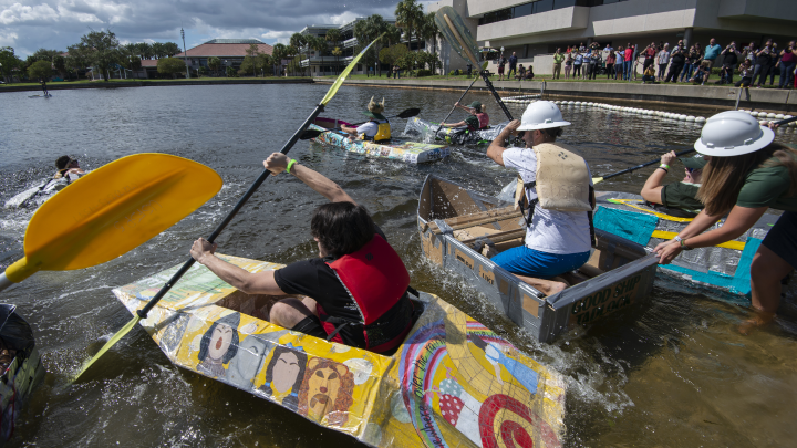 several people in cardboard boats with others looking on in the background