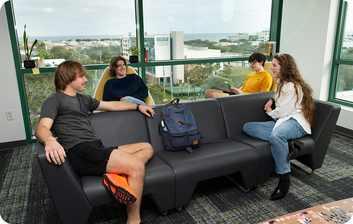 Four students lounging on a couch in casual conversation