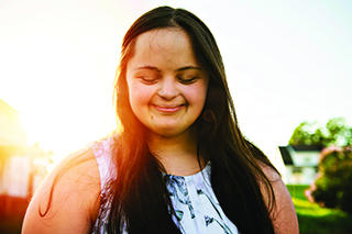 Woman smiling while looking down with the sun shining in the background