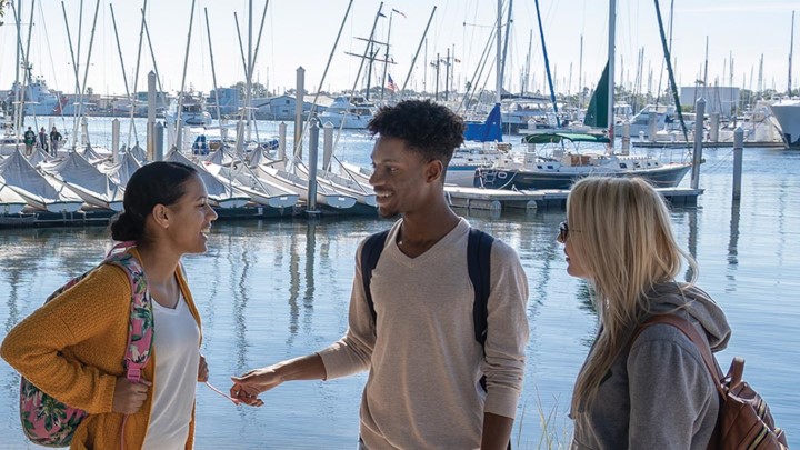 three students talking with boats in the background