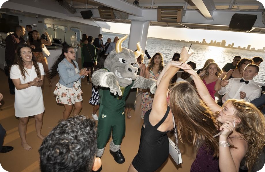 Group of students dancing with Rocky the Bull on a boat with St. Pete skyline in the background