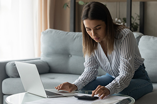 Student sitting on a couch using a calculator that's sitting on a coffee table with a laptop next to it