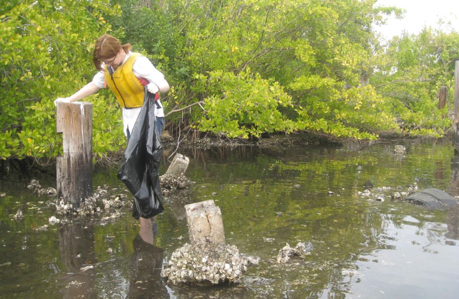 Woman with trashbag wading through brackish water
