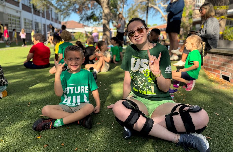 Student and young child sitting cross legged outside