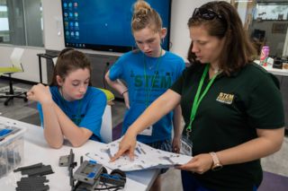 Teacher explaining robotics to two young students
