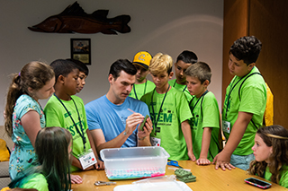 A teacher working on an object while surrounded by school aged children