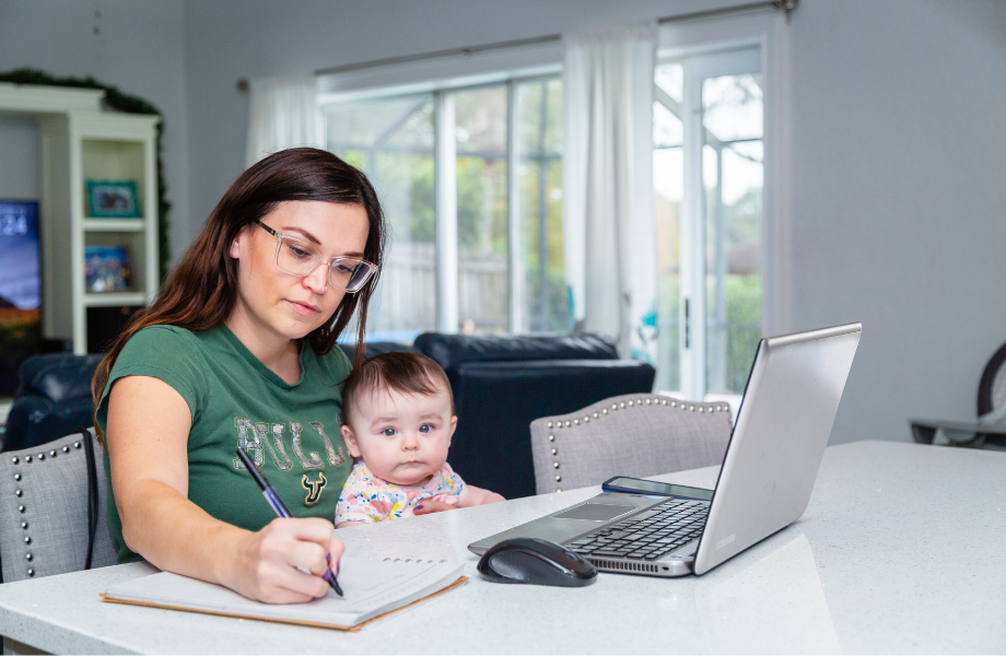 USF Student writing notes at counter, in front of laptop, while holding a baby