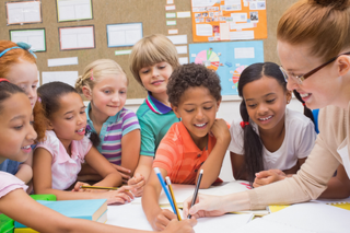 Teacher and students holding pencils on a piece of paper in front of them