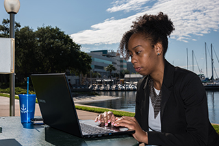 A student sitting outside of Bayboro Harbor working on a laptop