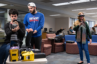 two male students examining a VR cube and one female student wearing VR goggles