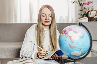 Student sitting beside a globe,  holding a notebook and pencil