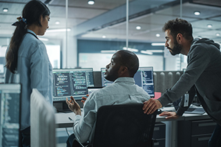 Three people in front of computer monitors.