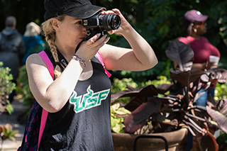 A student outside holding a camera up to her face, taking a photo of something off screen