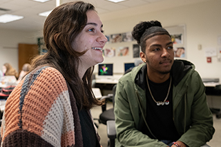 Two students sitting in a classroom looking at something outside the camera view