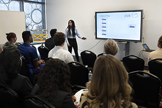 Student in front of the class talking while standing next to a monitor