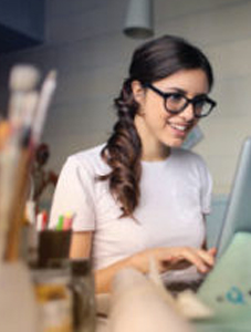 smiling young woman at computer with paint brushes in the foreground