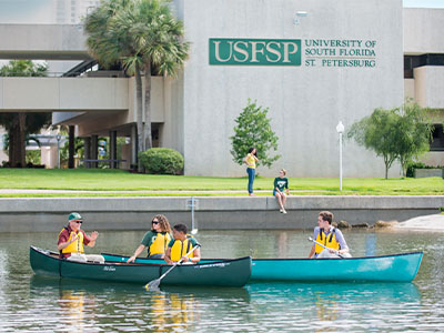 USF students holding paddles in a canoe.