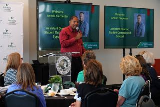 Man in a red shirt speaking to a groupd of alumni.