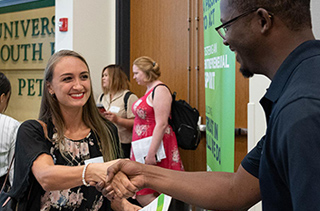 woman and man shaking hands at large meeting