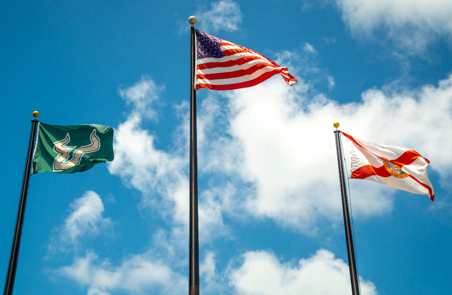 The USF, United States, and State of Florida flags flying with a background of blue skies and white clouds