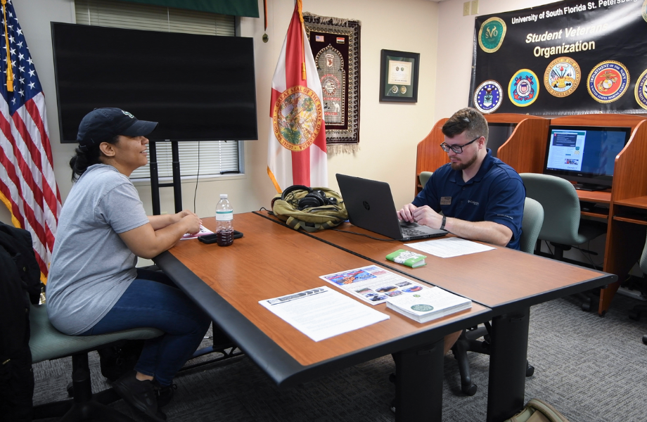 A woman sitting at a table across from a man who is looking at his laptop.