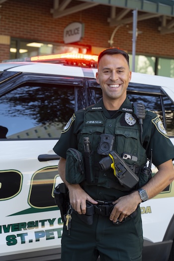 Officer smiling and standing in front of a police car with lights activated on top