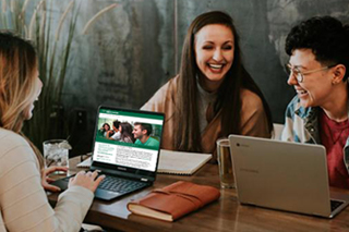 three students sitting at a table working on laptops