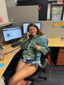 Student sitting on chair talking on phone and holding stuffed animal.