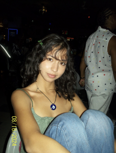Student wearing green shirt and blue necklace looking directly at camera.