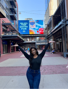 Student posing in city plaza holding up both arms.