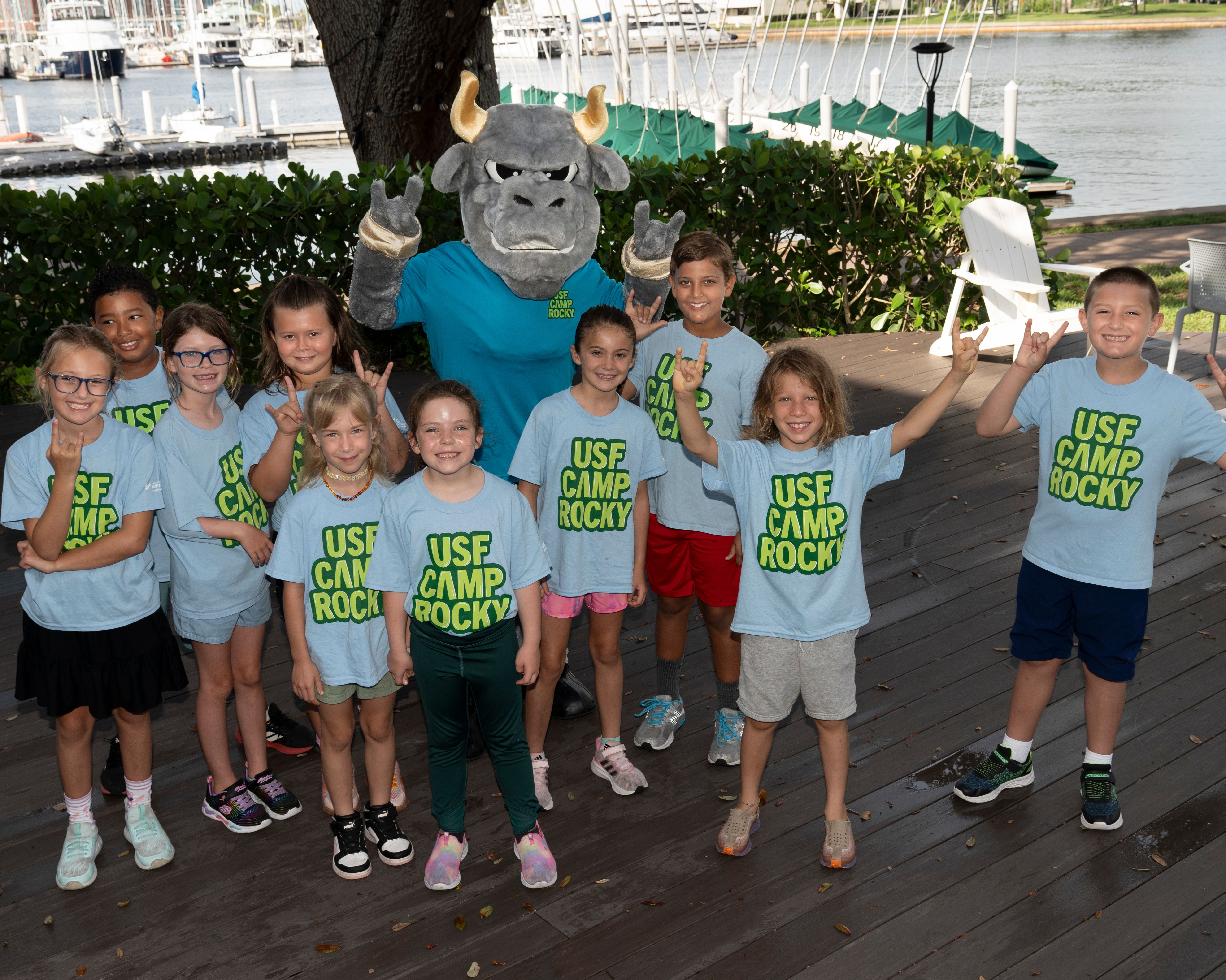 Group of students standing and posing next to Rocky the Bull wearing "USF Camp Rocky" tee shirts