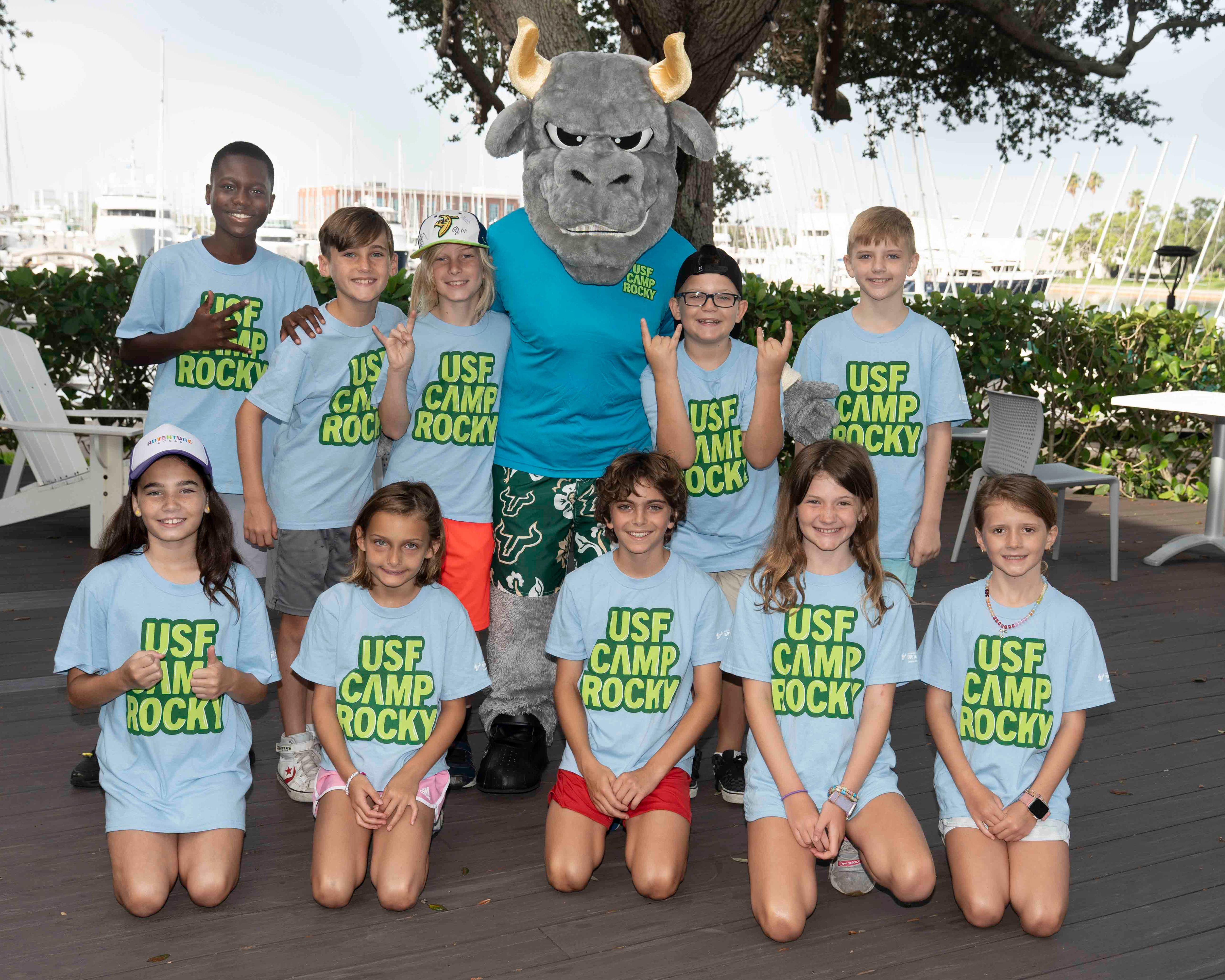 Two rows of students posing with Rocky the Bull wearing "USF Camp Rocky" tee shirts
