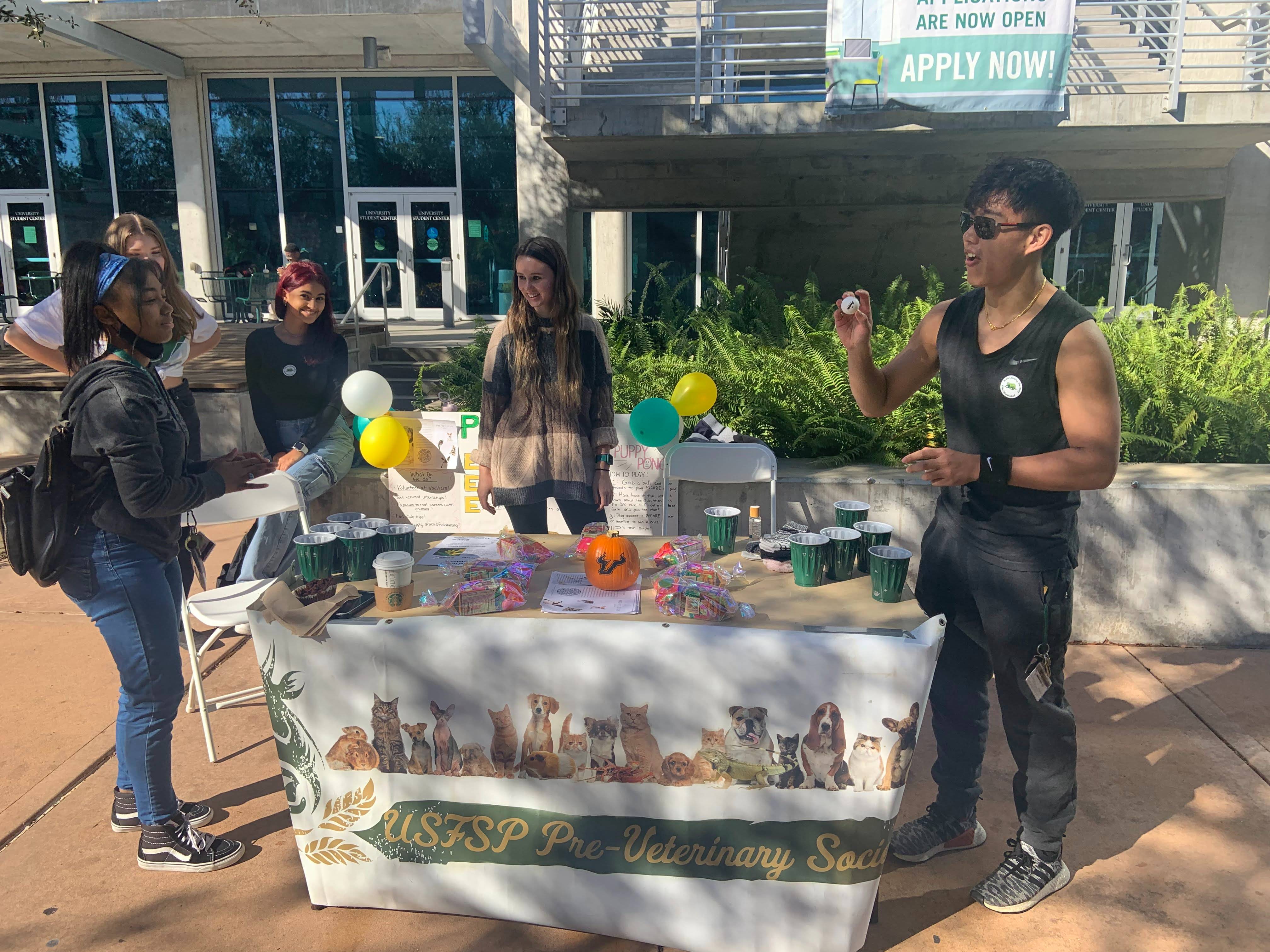 The USFSP Pre-Veterinary Society tables at Harbor Market. Students stand on each side of the table playing a game. 