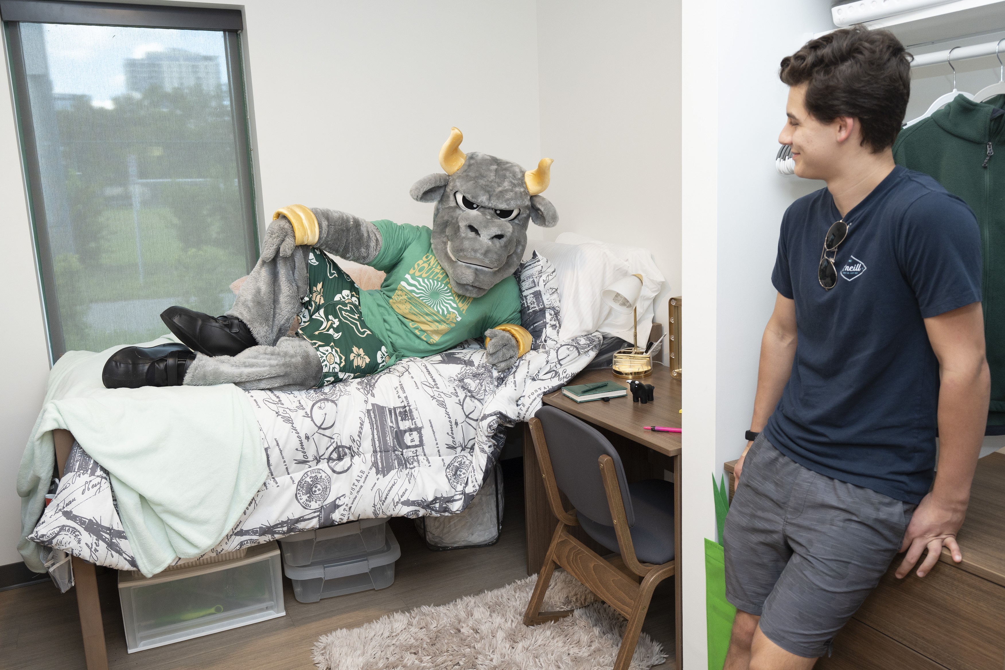 Rocky the Bull lounges on bed while student looks at him. 