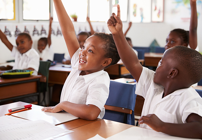 students sitting in a classroom raising their hands