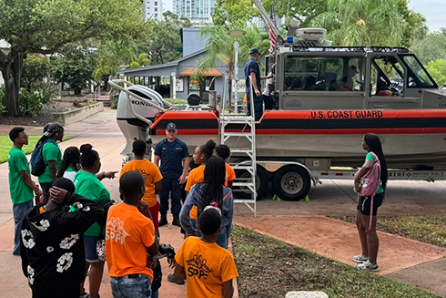 coast guard board on a trailer with a group of young students listening to someone speak