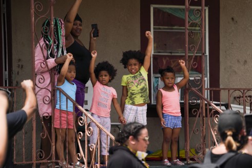 a group of young girls raising their fists in support as hundreds of people participate in a march by their home