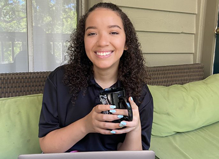 Andrea Rodriguez Campos sitting on a front porch with a laptop while holding a coffee mug