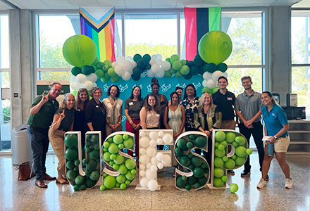 People posing in front of a USFSP sign filled with balloons.