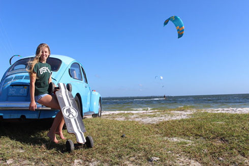 Entrepreneurship Student Makenzie Black holding a cargo trailer while leaning against a car parked on a beach